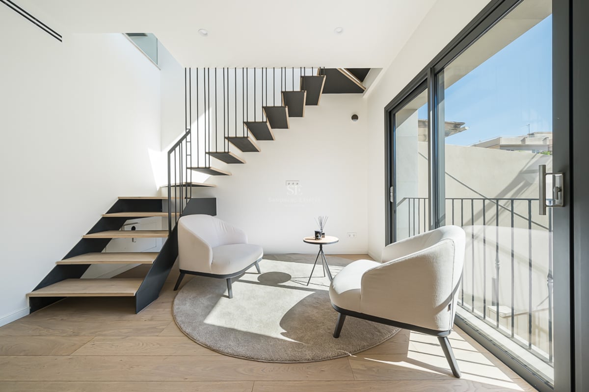 Contemporary floating staircase with oak treads next to two cream armchairs and large glass sliding doors.