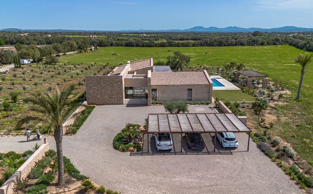 Luftaufnahme einer modernen Steinvilla mit Kiesauffahrt, Carport und Pool mit Blick auf die grüne Landschaft.