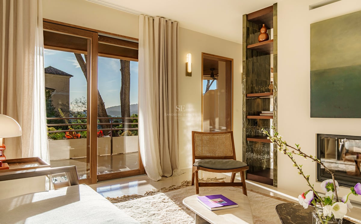 Lichtdurchflutetes Wohnzimmer mit Korbstuhl, Holzschiebetüren zum Balkon und eingebautem Kamin.