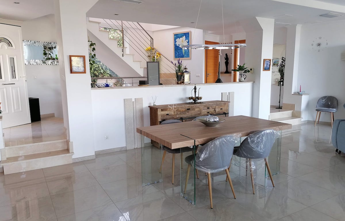Salle à manger moderne avec table en bois, pieds en verre, sol en marbre et escaliers en arrière-plan.