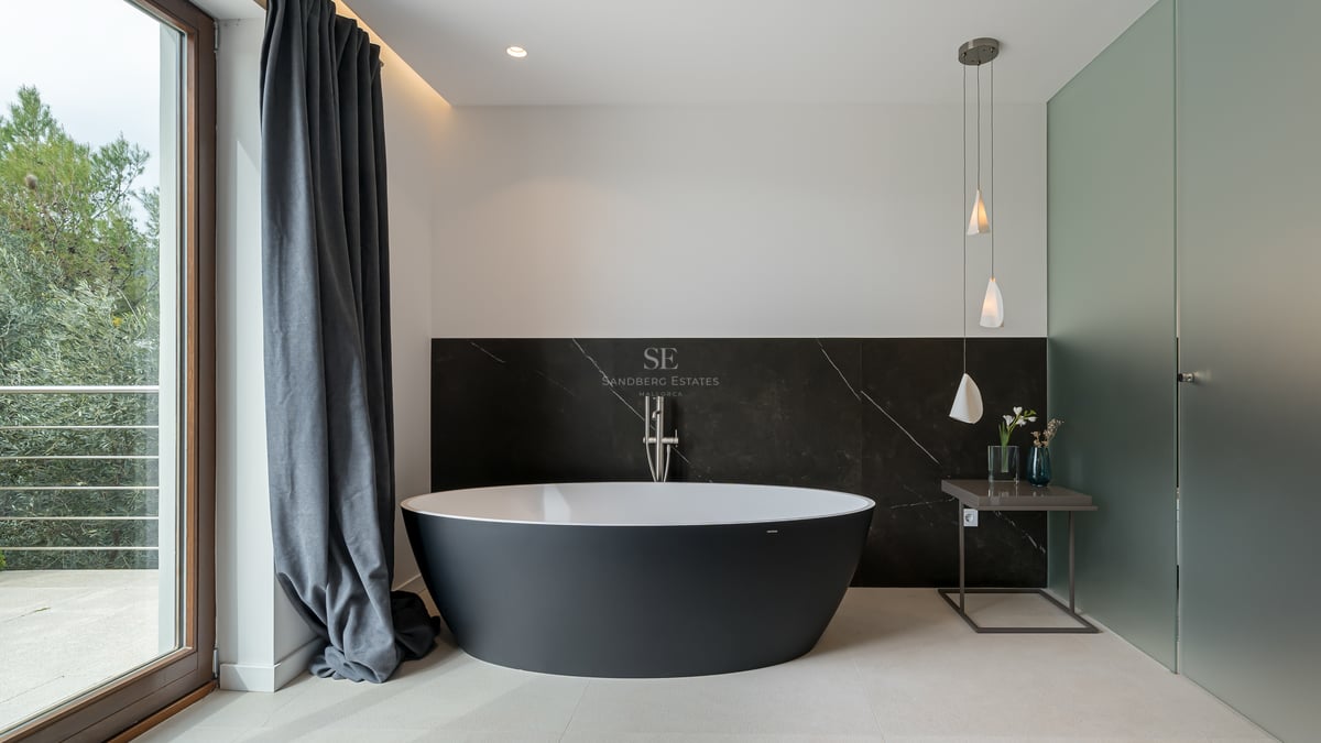Salle de bain moderne avec baignoire îlot noire ovale devant un mur en marbre sombre et lumière naturelle.