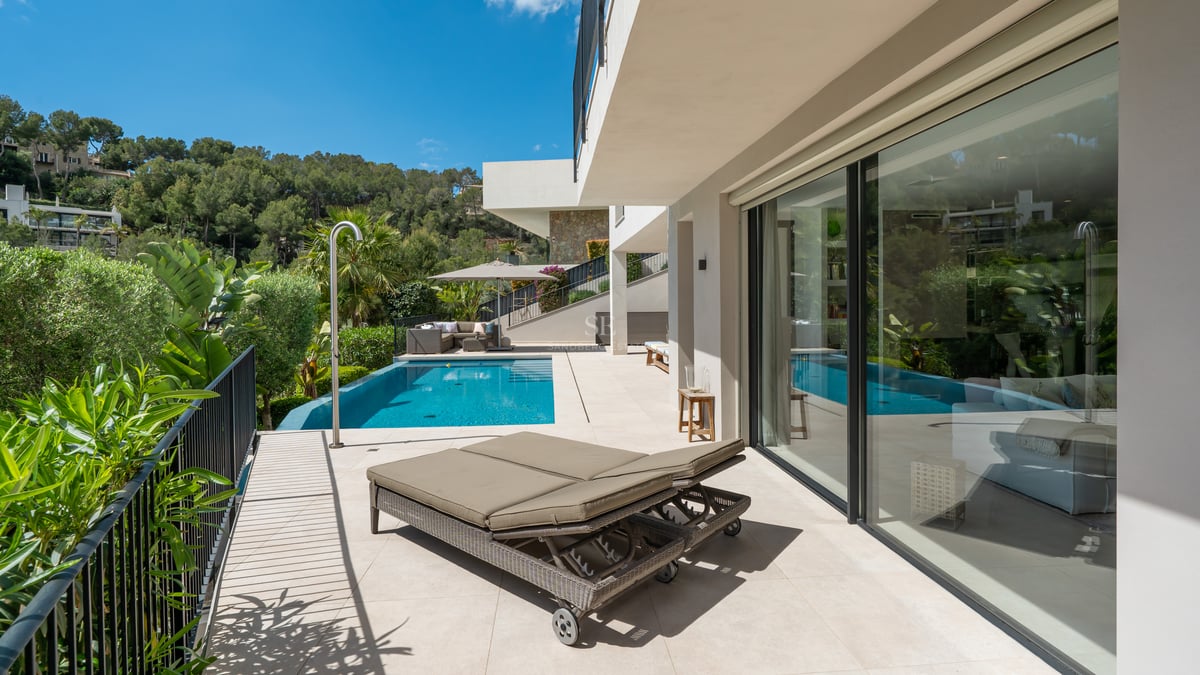 Vue sur la piscine avec terrasse en bois, chaises longues, parasols et jardin luxuriant. Design moderne avec éclairage naturel.