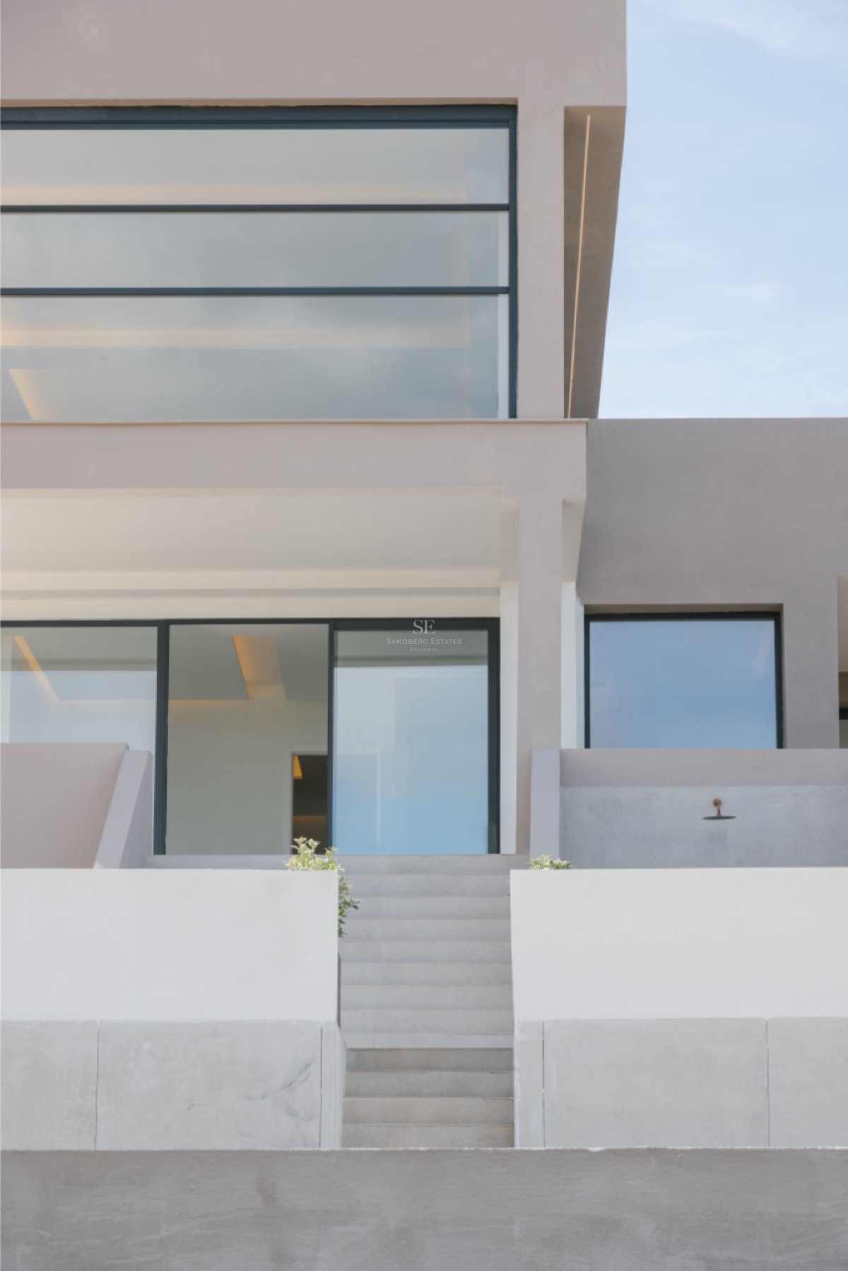 Außenansicht einer zeitgenössischen Villa mit Betontreppen, die zu großen Glasfronten und neutralen Wänden führen.