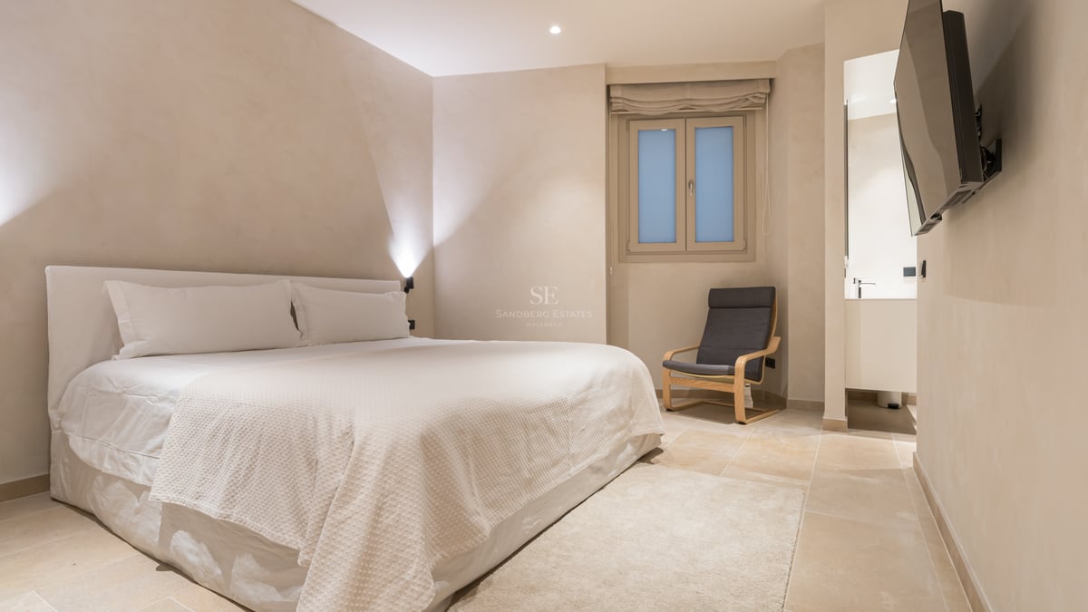 Chambre minimaliste avec sol en pierre naturelle, murs crème, grand lit et aperçu de la salle de bain.