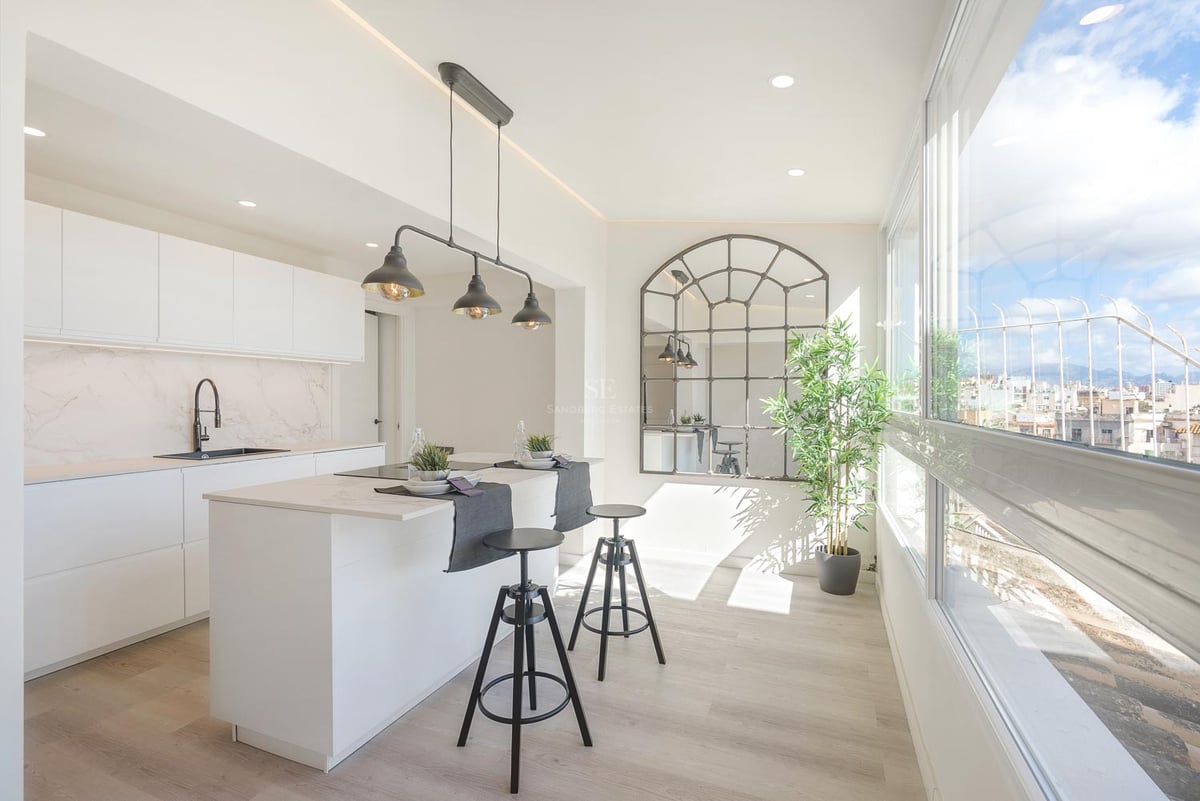 Helle moderne Küche mit weißer Kochinsel, schwarzen Barhockern und großen Fenstern mit Blick auf die Stadt.