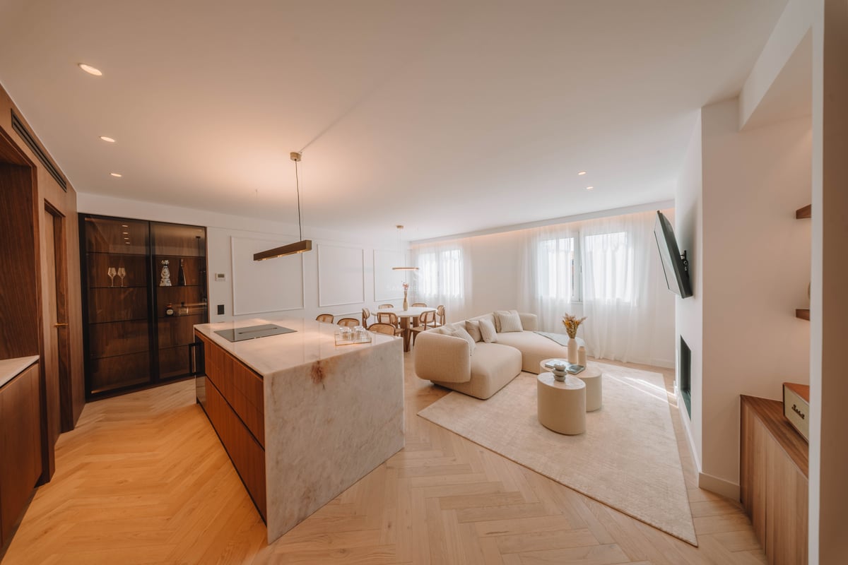 Salon lumineux à aire ouverte avec un grand îlot de cuisine en marbre, un canapé beige incurvé et un parquet en chevrons.