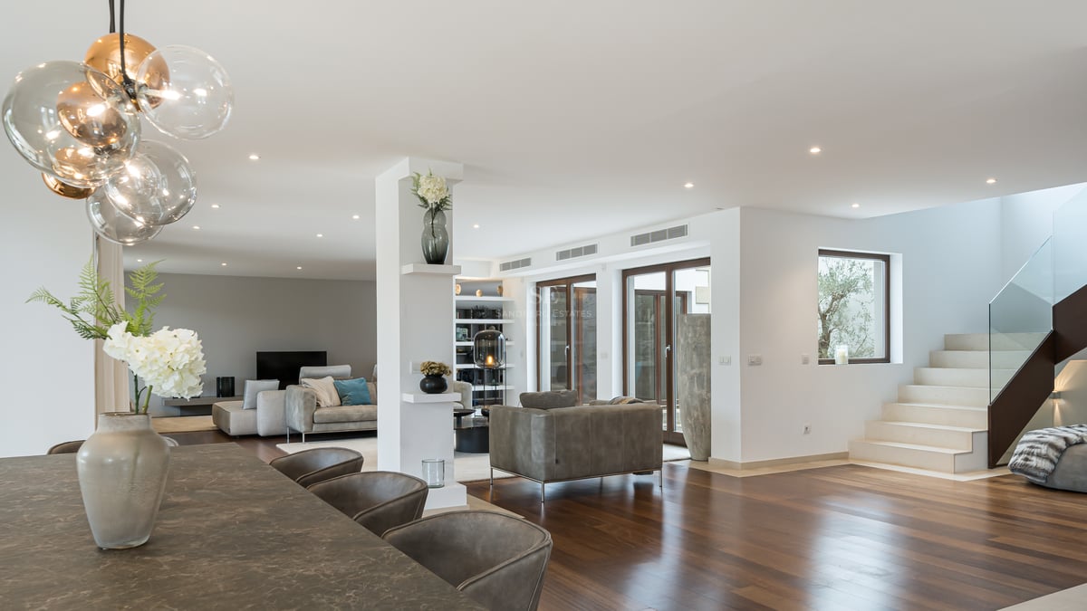 Intérieur spacieux avec parquet foncé, table de salle à manger en pierre, luminaire globe et escalier en pierre blanche.