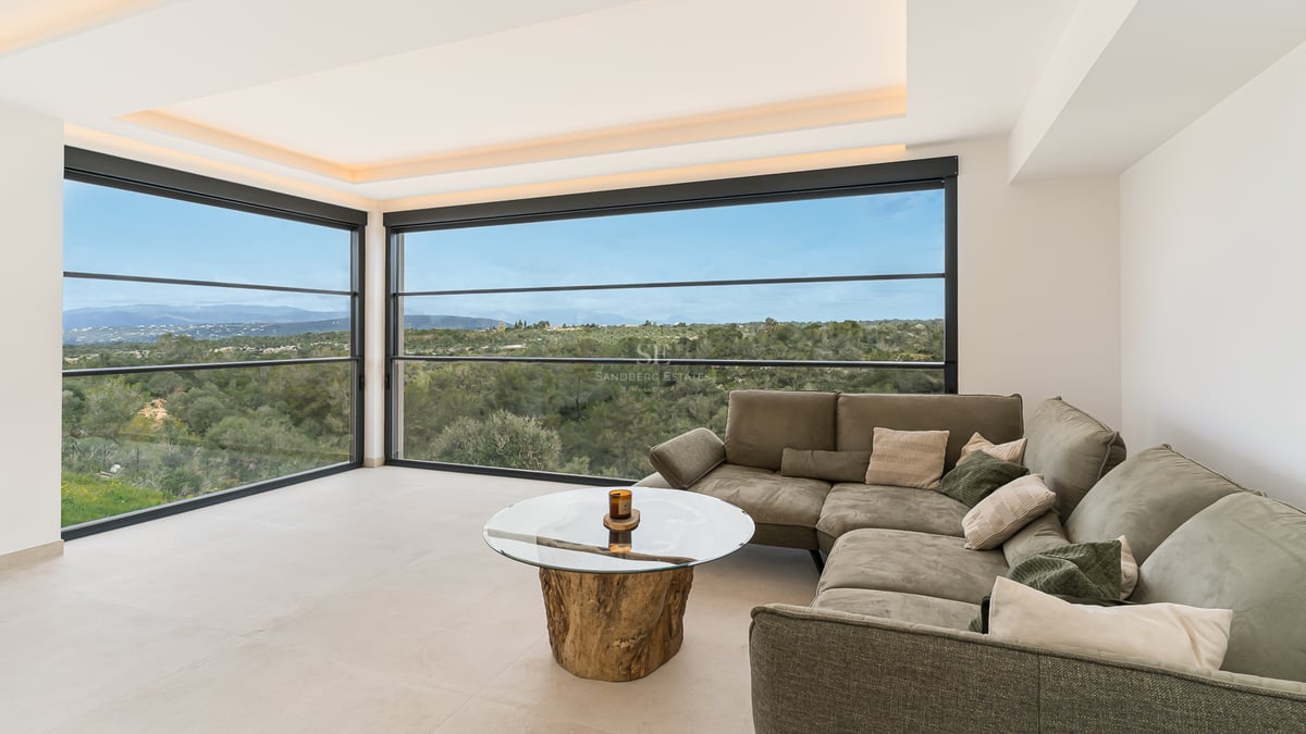 Zeitgenössisches Wohnzimmer mit grauem Sofa, Holz-Couchtisch und großen Fenstern mit Blick auf grüne Landschaft.