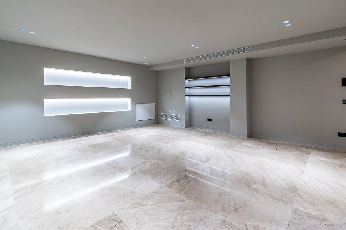Pièce moderne vide avec sol en marbre poli, murs gris et éclairage LED intégré dans des niches murales.