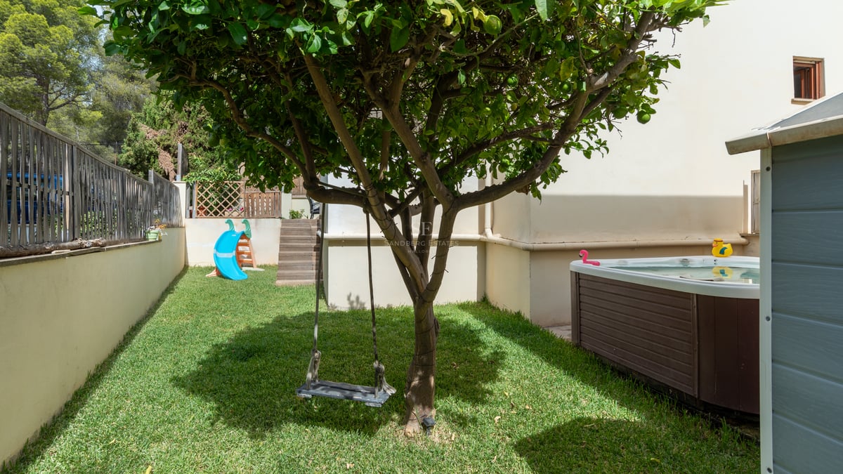 Jardin avec pelouse, balançoire dans un arbre, toboggan bleu et jacuzzi extérieur habillé de bois.