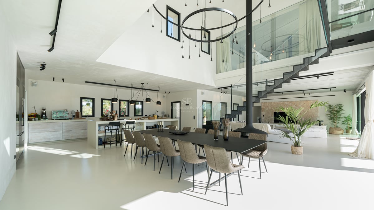 Modern matsal med svart långbord, hängande öppen spis och entresolplan i glas.