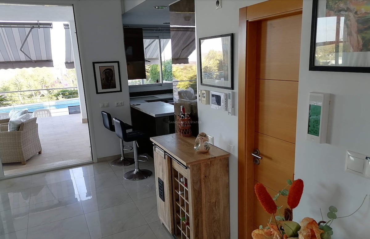 Vue intérieure d'un espace de vie moderne avec cave à vin, ouvrant sur une terrasse ensoleillée et une piscine.