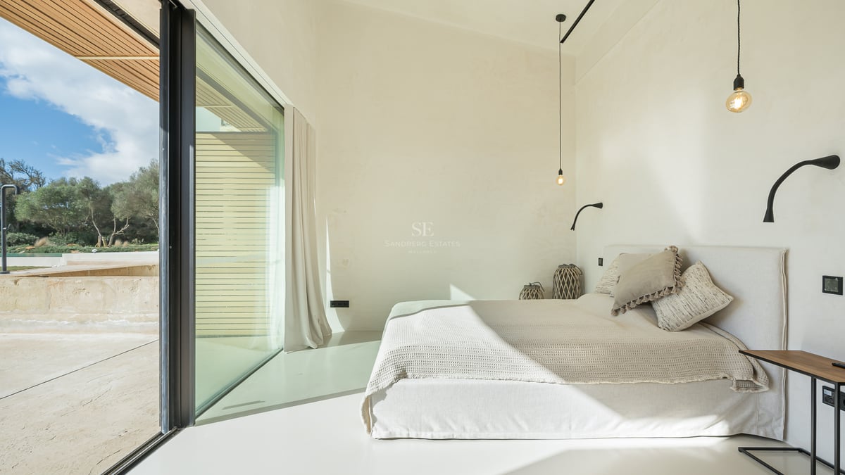 Ljust minimalistiskt sovrum med vit säng, stora glaspartier och privat balkong.