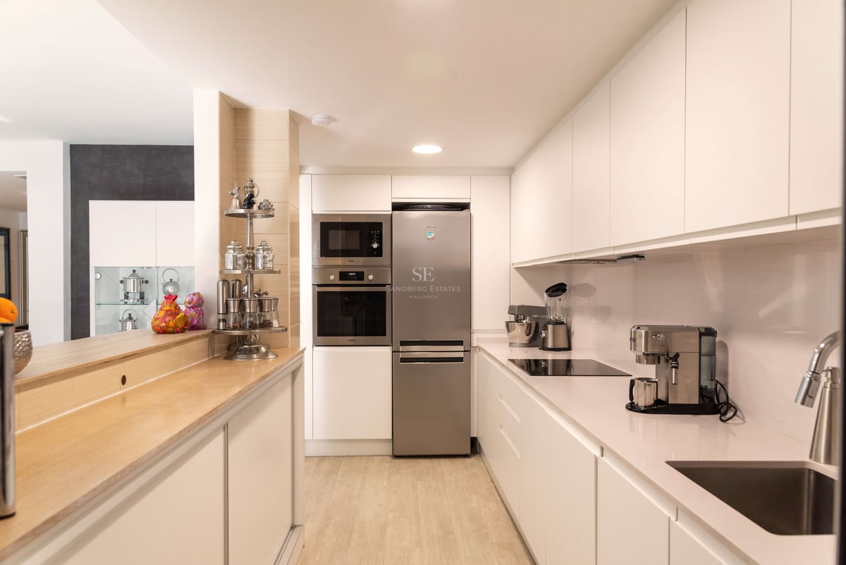 Saubere, moderne Küche mit weißen Schränken, Edelstahlgeräten und einer Frühstücksbar aus hellem Holz.