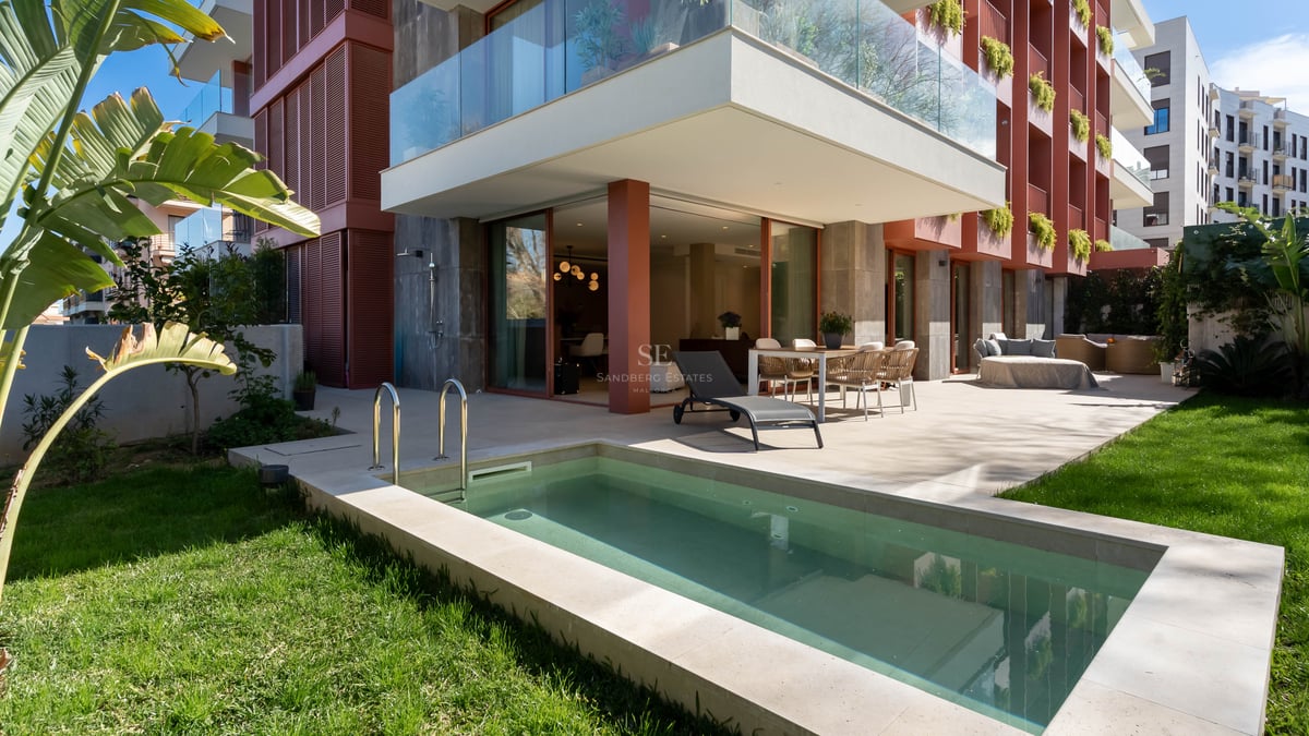 Luxury terrace with private plunge pool, outdoor dining set, sun lounger, and green lawn by a modern apartment building.