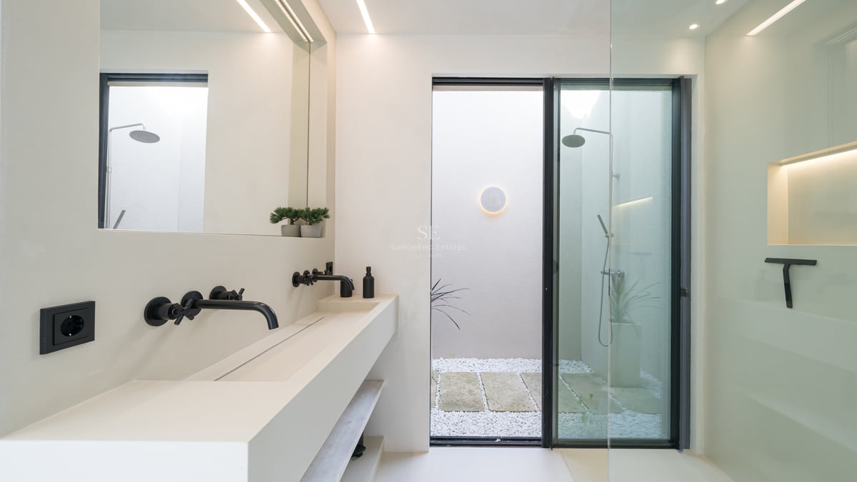 Modernt vitt dubbelhandfat med mattsvarta kranar och walk-in-dusch som vetter mot en innergård med stenar.