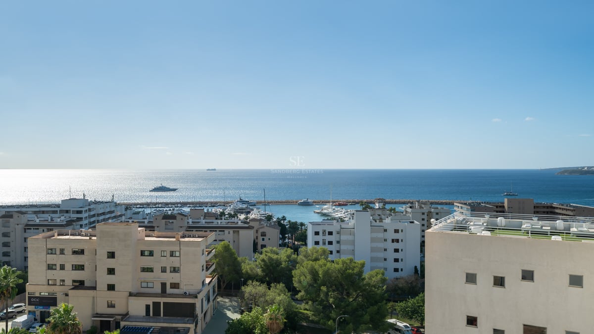 High-angle view of a coastal city, a yacht-filled marina, and the vast blue Mediterranean Sea under a bright sky.