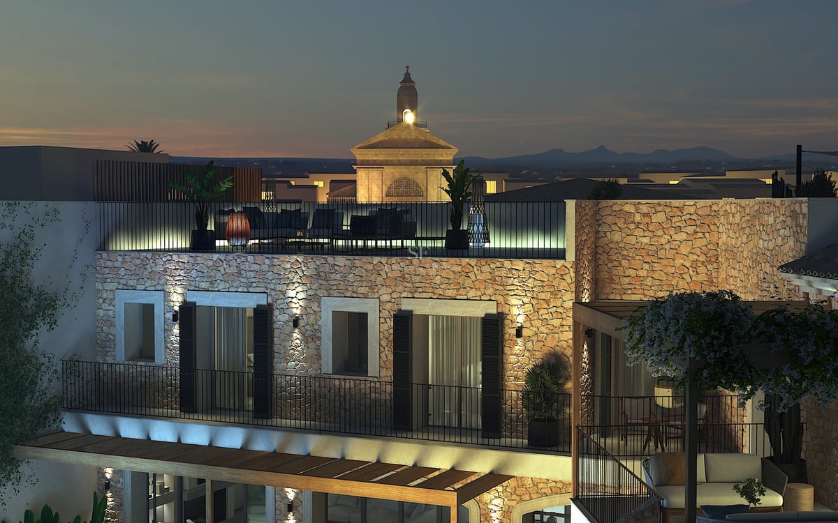 Vue nocturne d'une villa méditerranéenne avec murs en pierre éclairés et terrasse de toit dominant le village.