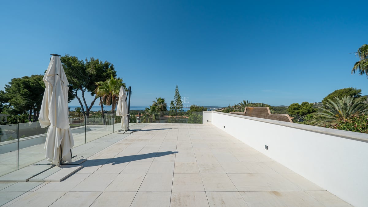 Grande terrasse en pierre blanche avec garde-corps en verre surplombant la mer Méditerranée.