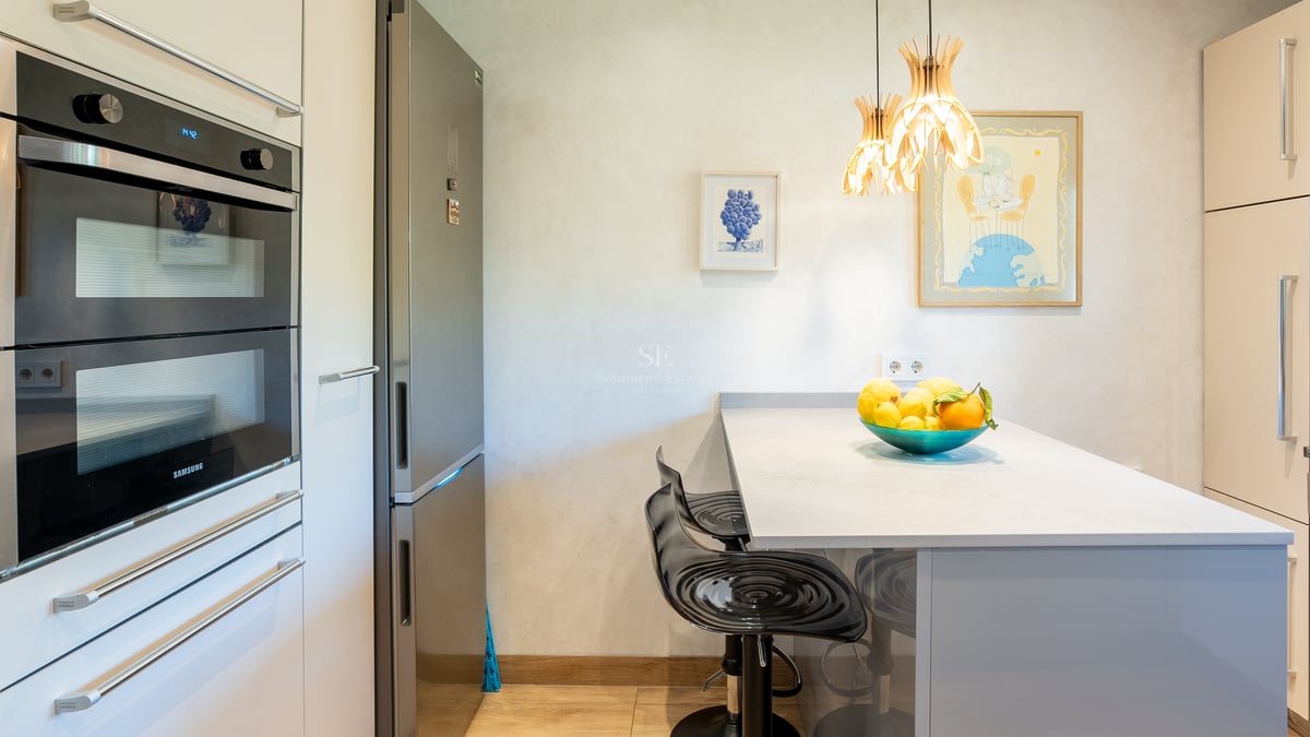 Samtida kök med Samsung dubbelugn, kylskåp i rostfritt stål och frukostö med svarta barstolar.