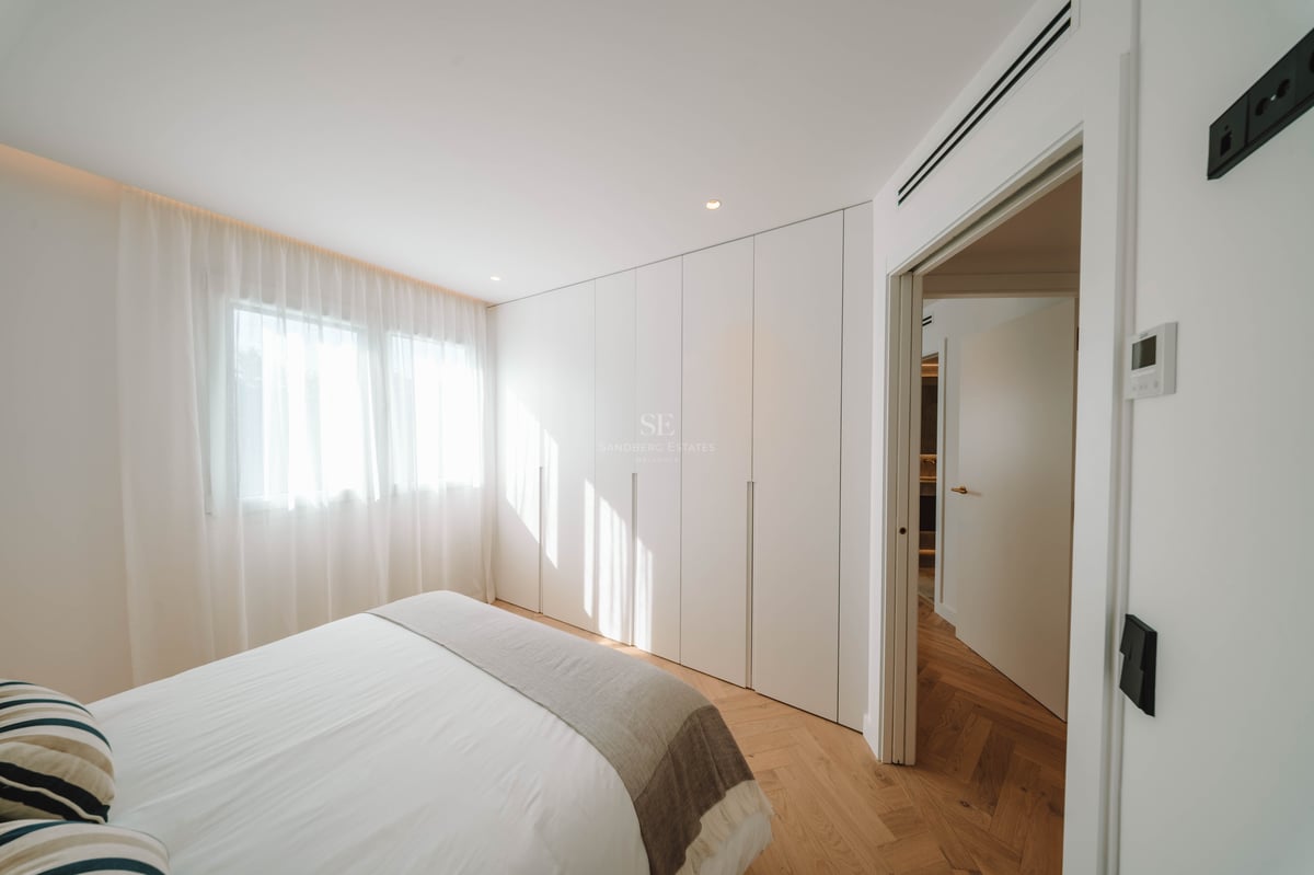 Chambre lumineuse avec parquet en point de Hongrie, grands placards blancs, lit avec draps blancs et rideaux voilages.