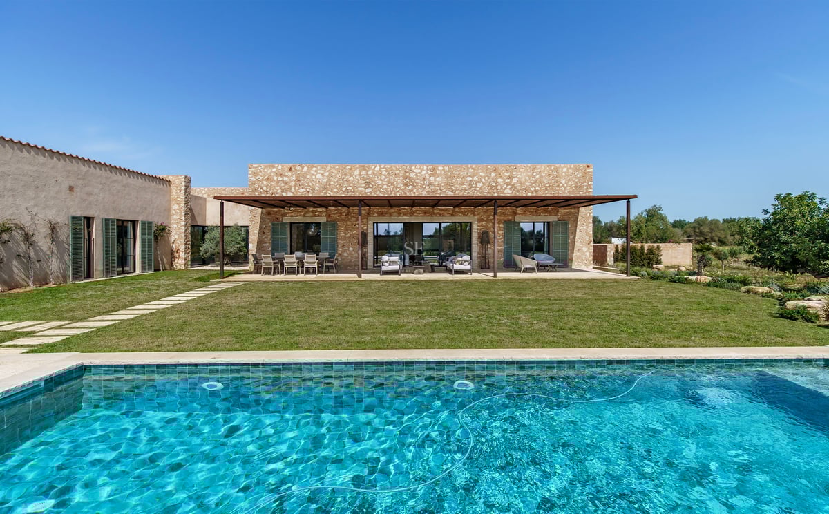 Luxusvilla-Exterieur mit türkisfarbenem Pool, Rasenfläche und Natursteinfassade unter klarem blauem Himmel.