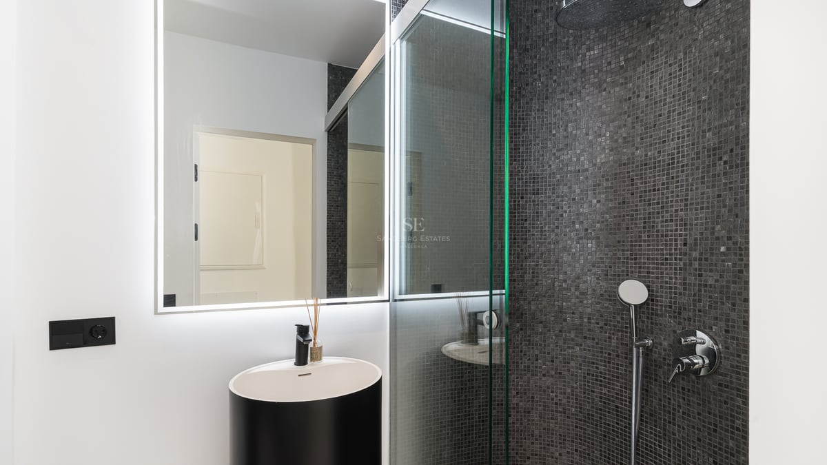 Modernt badrum med svart cylindriskt tvättställ, LED-spegel och dusch med mörkgrå mosaik.