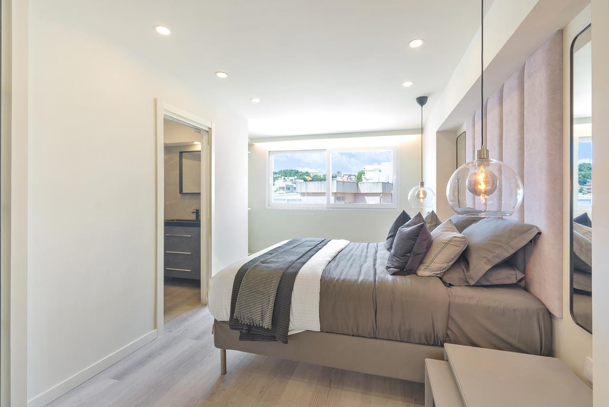 Modernes Schlafzimmer mit rosa Samtkopfteil, Glaspendelleuchten und Zugang zum En-Suite-Badezimmer.