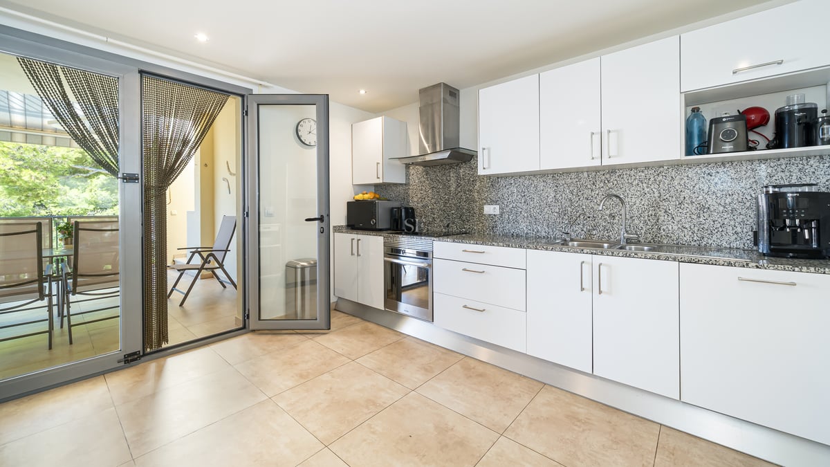 Modernt vitt kök med bänkskivor i granit och glasdörr ut mot en möblerad terrass.