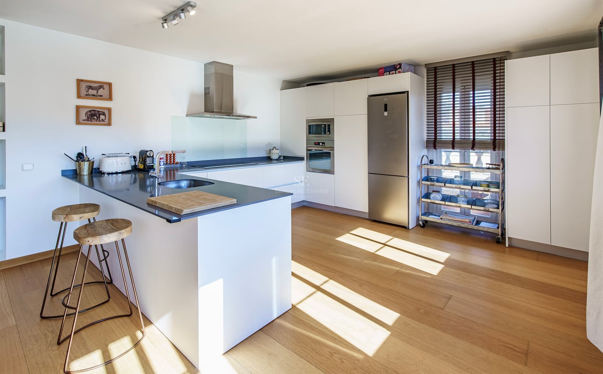 Modernt designat kök med vit köksö, grå bänkskiva, trägolv och vitvaror i rostfritt stål.