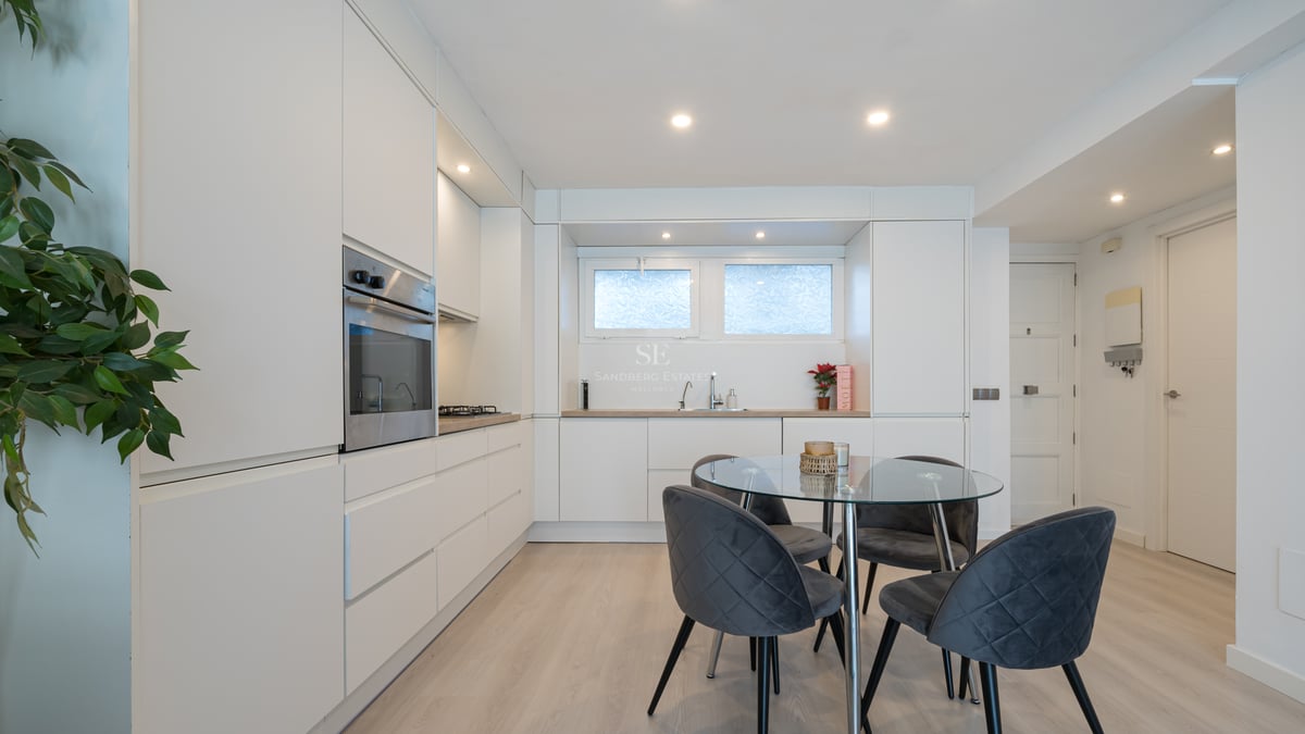 Clean white minimalist kitchen featuring handleless cabinetry, glass dining table, and grey velvet chairs.