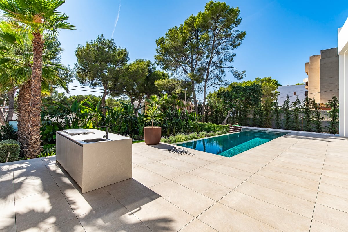 Terrasse en pierre avec îlot de cuisine minimaliste à côté d'une piscine turquoise et jardins tropicaux.