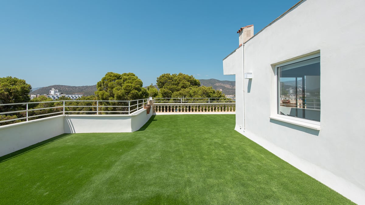 Grande terrasse sur le toit avec gazon synthétique, garde-corps en métal et vue sur les collines.
