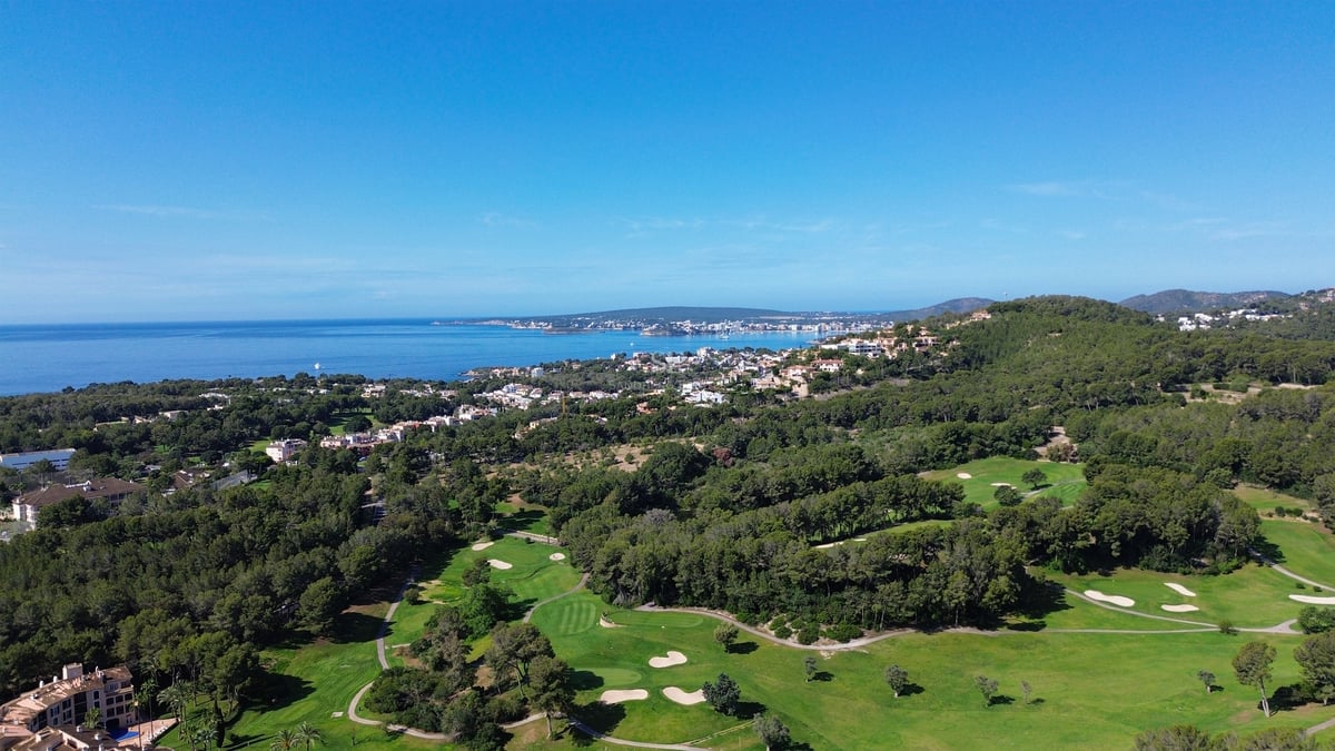 Vue aérienne d'un parcours de golf verdoyant bordé d'une forêt de pins et de la mer Méditerranée.