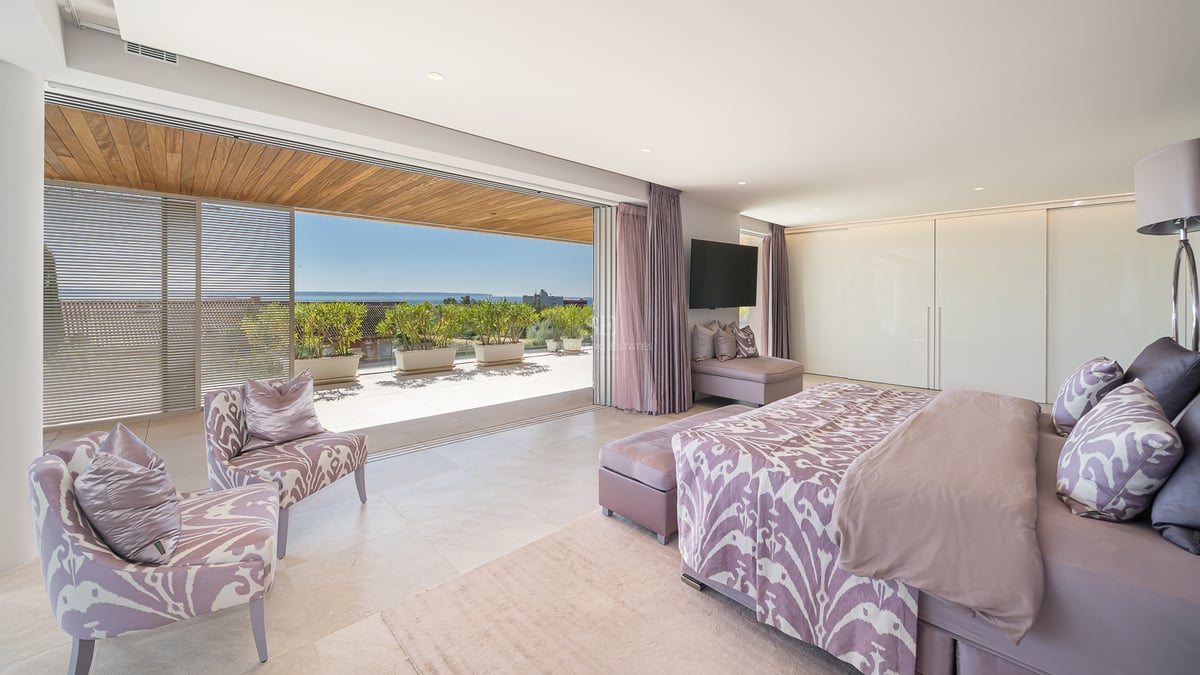 Luxuriöses Schlafzimmer mit Doppelbett, Zugang zur Holzterrasse und Meerblick durch große Glasschiebetüren.