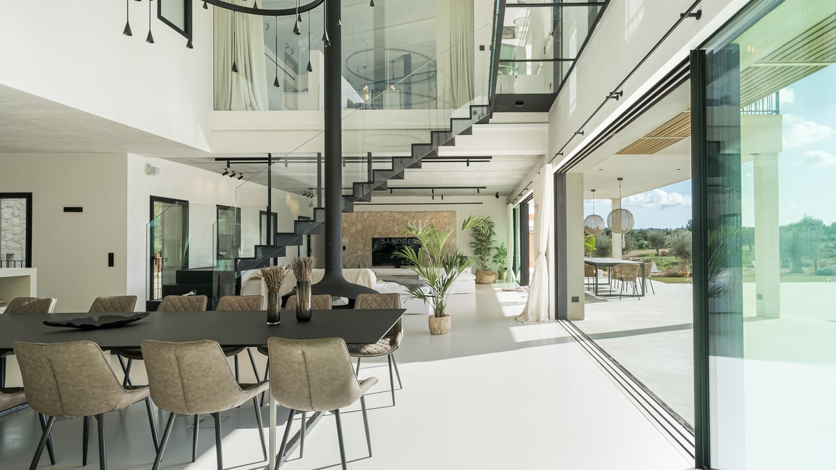 Modernt vardagsrum med öppen planlösning, svart svävande trappa, dubbel takhöjd och stora glaspartier.