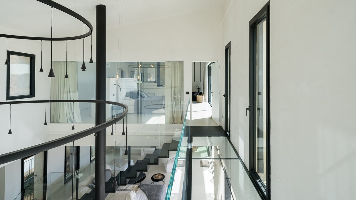 Modern hall med gångbro i glas, svart trappa och stora fönsterpartier i en lyxig villa.