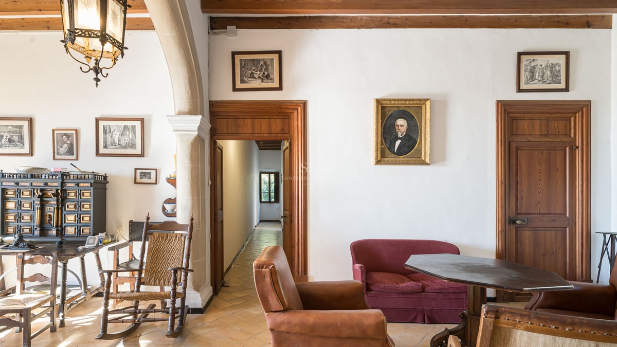 Salon classique avec meubles anciens, sol en terre cuite, canapé en velours rouge et portraits aux murs.