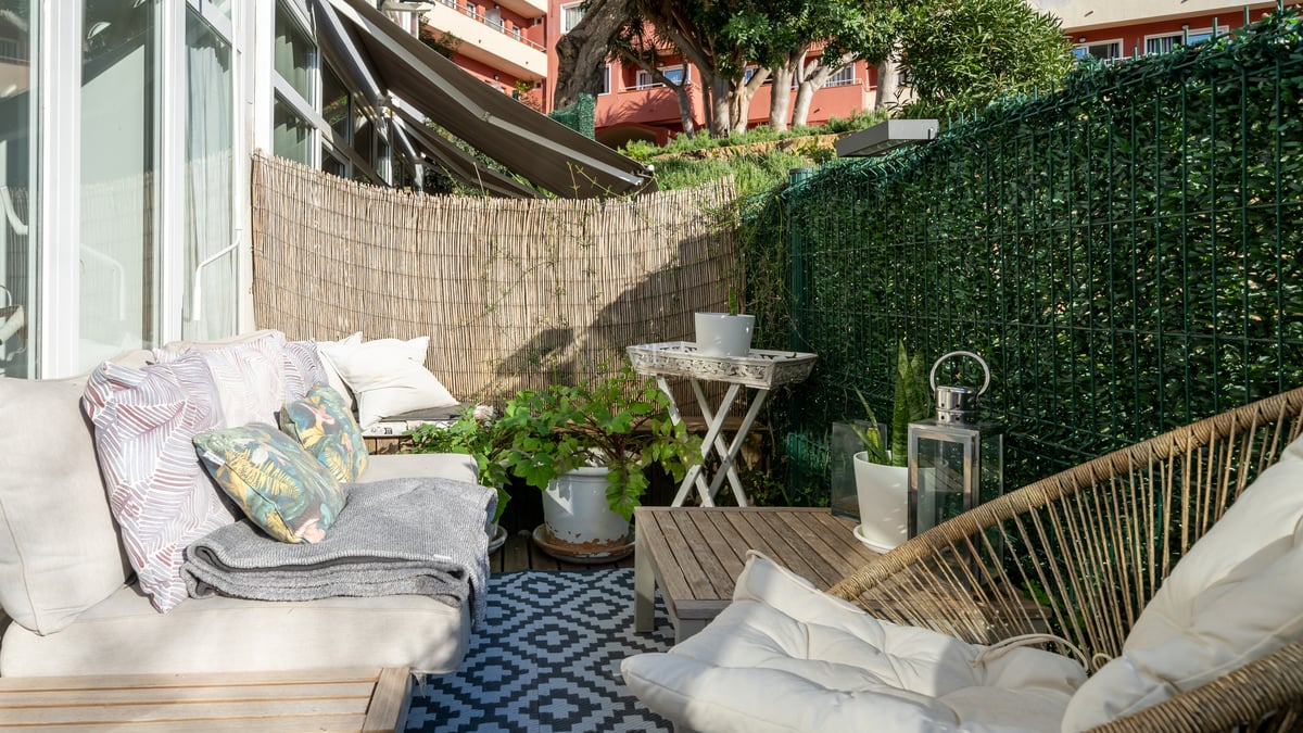 Sunny terrace featuring comfortable sofas, a geometric rug, and bamboo privacy screening in a coastal setting.