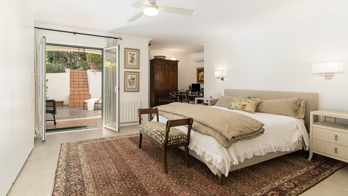 Spacious master bedroom with a large bed, oriental rug, and glass doors opening to a terracotta patio.