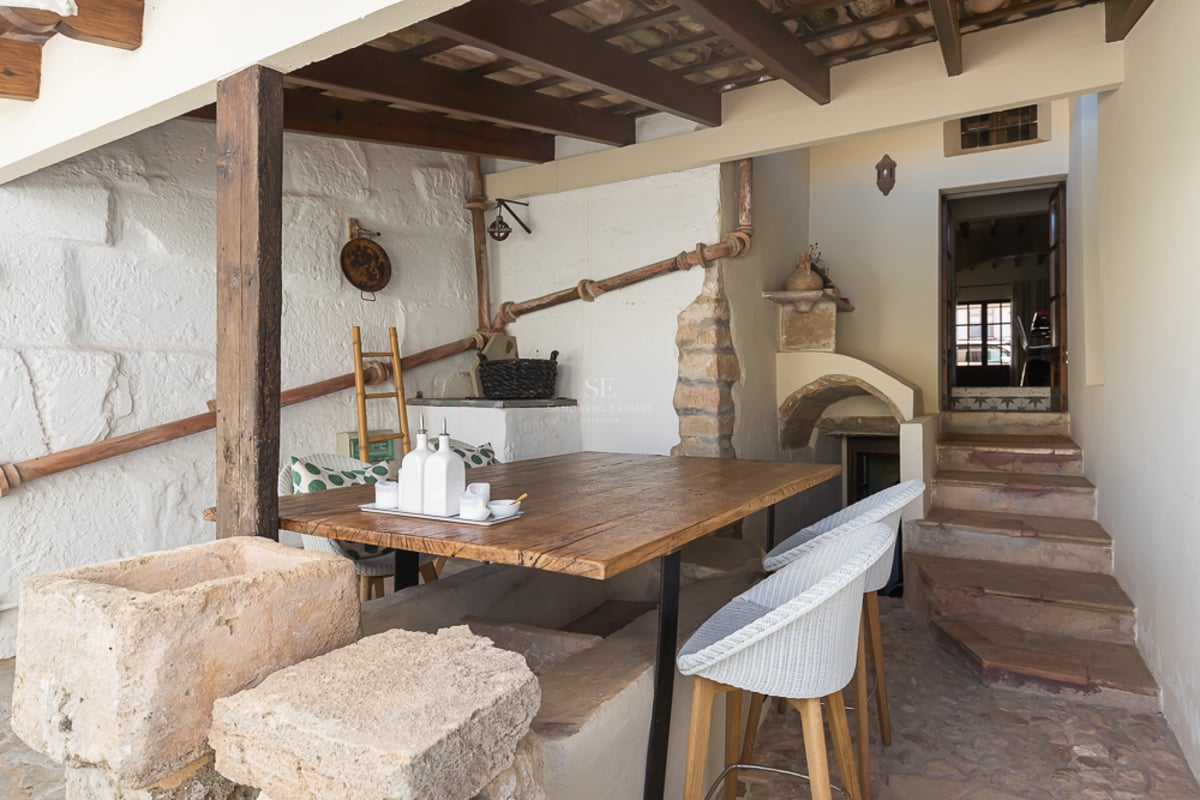 Coin repas extérieur rustique avec table en bois, murs en pierre, poutres apparentes et escaliers en pierre.