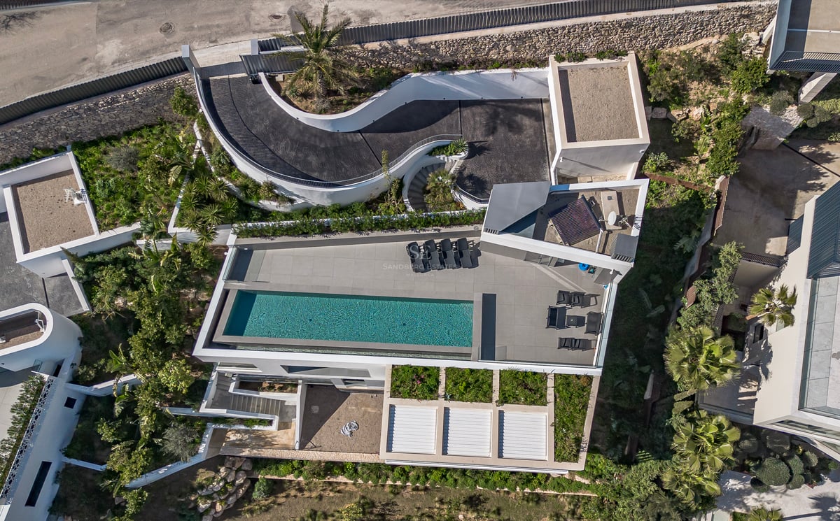 Vue aérienne d'une villa moderne avec piscine rectangulaire, terrasse avec chaises longues et rampe d'accès courbe.