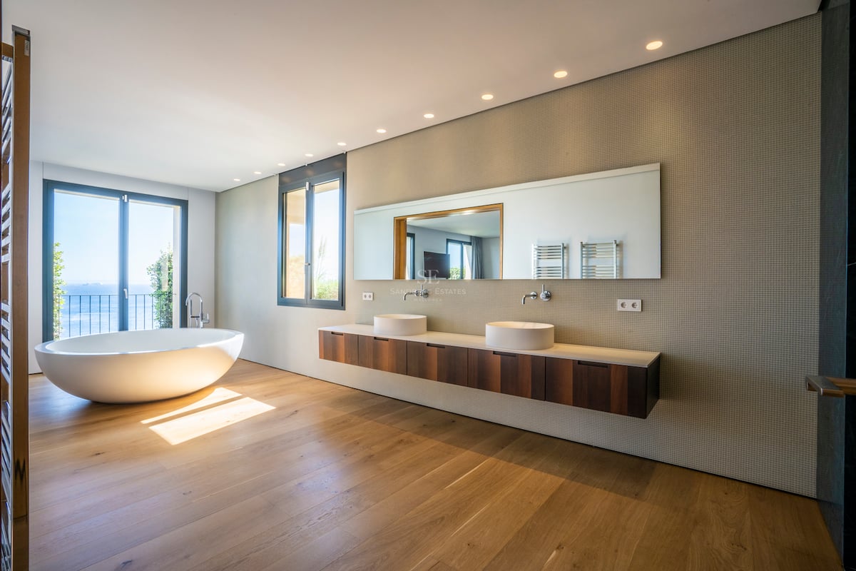 Modernes Badezimmer mit freistehender Badewanne, Eichenparkett, Doppelwaschtisch und Meerblick durch Glastür.