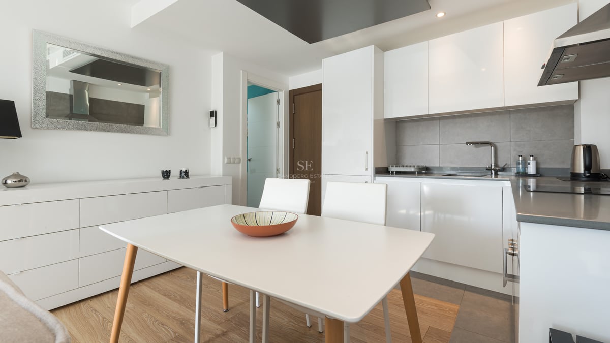 Cuisine moderne lumineuse avec des placards blancs, une crédence grise et une table à manger blanche.