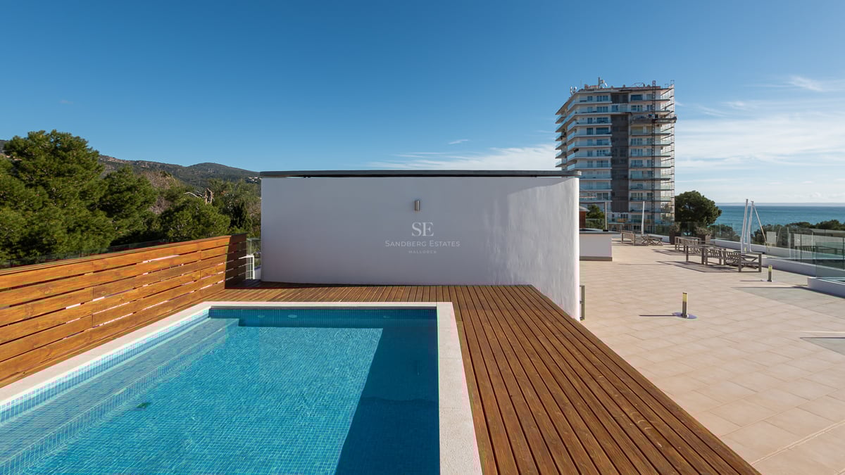 Piscine moderne sur le toit avec terrasse en bois, vue sur la mer et les montagnes sous un ciel bleu clair.