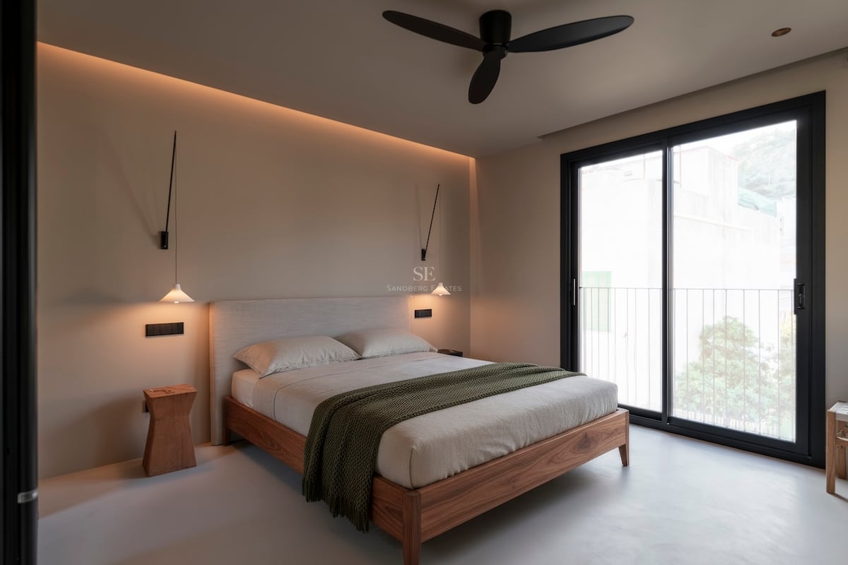 Chambre moderne avec lit en bois, suspensions design et porte vitrée coulissante ouvrant sur un balcon.