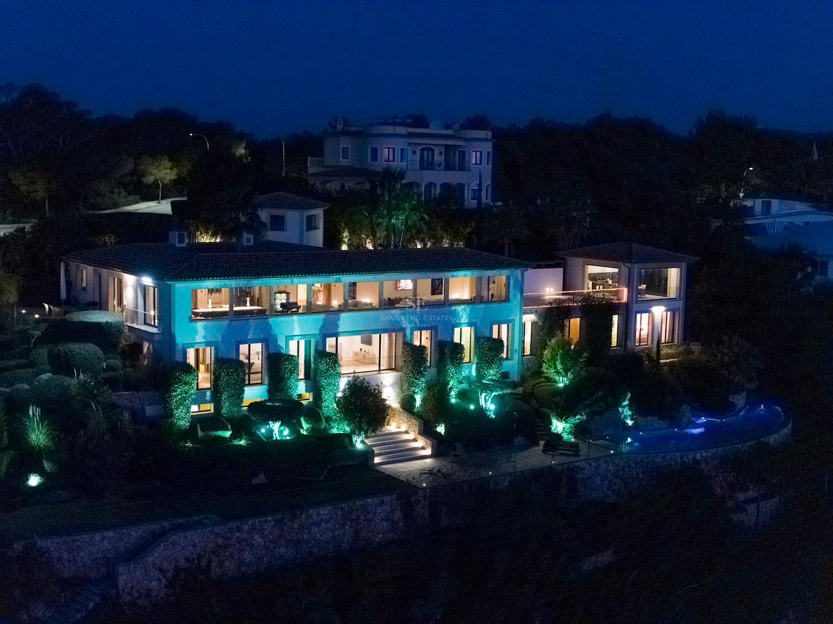 Abendliche Außenansicht einer zweistöckigen Luxusvilla mit beleuchteten Fenstern, Pool und Gartenanlage.