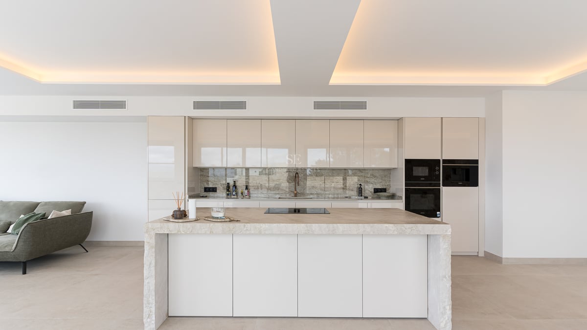 Minimalistische weiße Küche mit Marmorinsel und indirekter Deckenbeleuchtung in einer Luxusvilla.