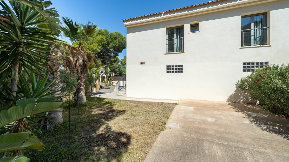 Exteriör av en tvåvåningsvilla i krämvitt med tegeltak och palmer under en klarblå himmel.