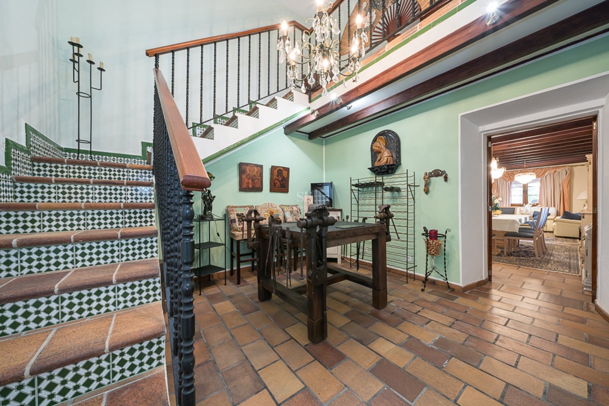 Hall d'entrée spacieux avec sol en terre cuite, escalier en fer forgé orné d'azulejos et poutres apparentes.